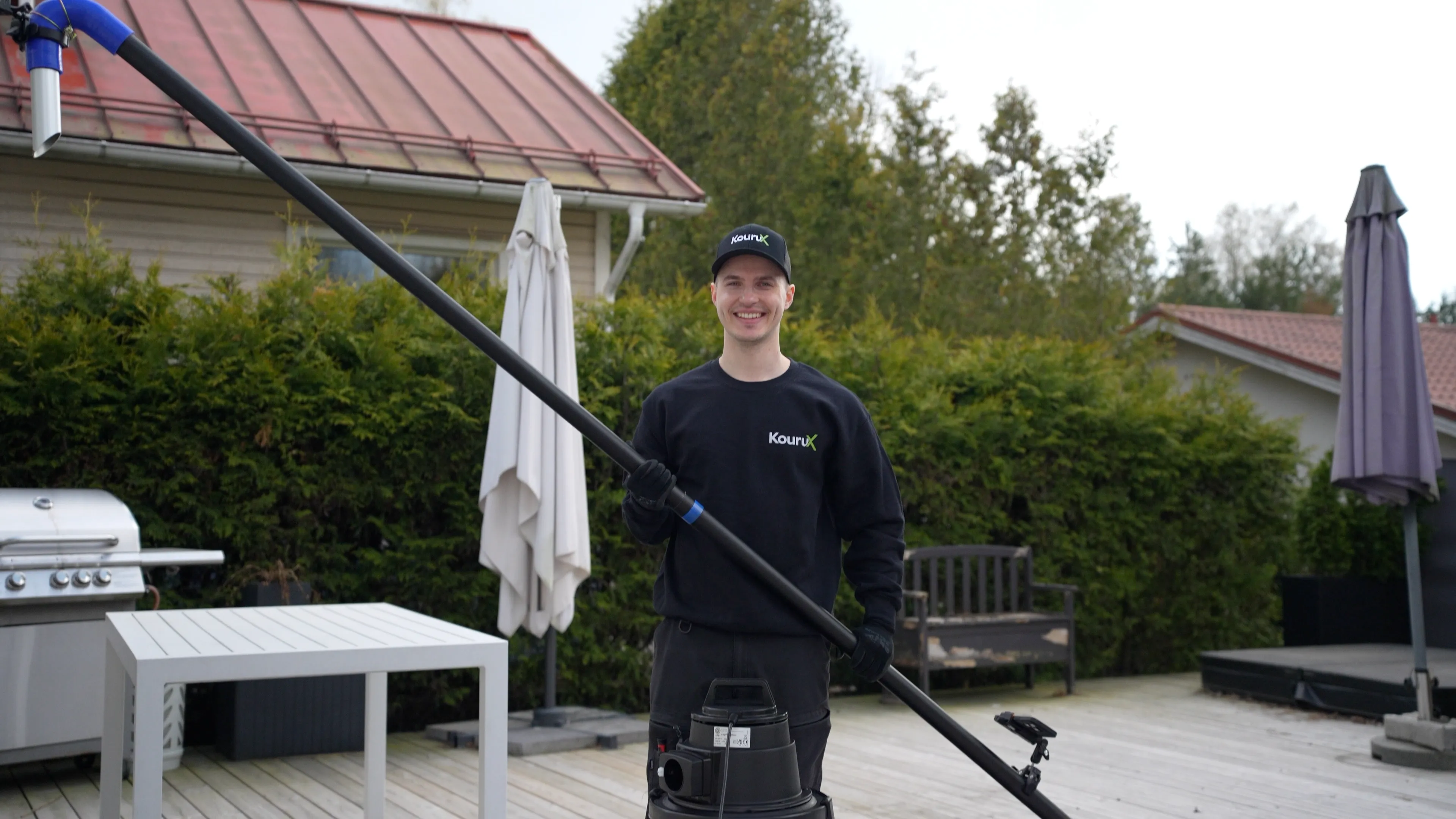 KouruX tekijä hymyilee ränni-imurin kanssa omakotitalon pihalla